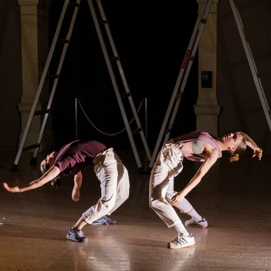 Two LEGS performers face each other in acrobatic move with backs stretched backwards and arms reaching behind
